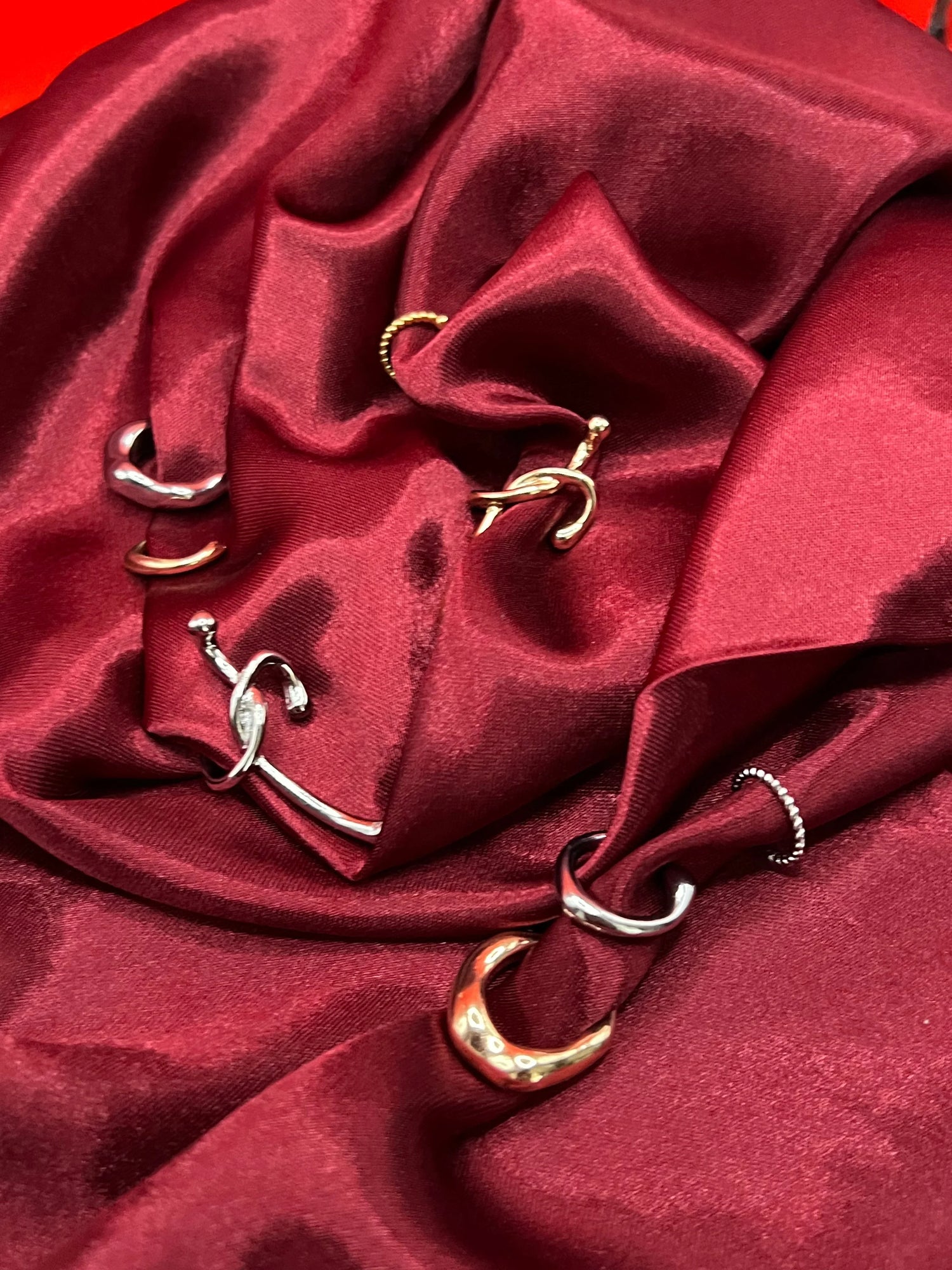 Anelli artigianali in acciaio inox LUEUR su tessuto rosso, design moderno e dettagli eleganti