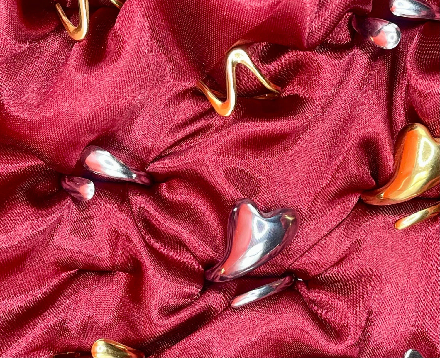 Gioielli artigianali in acciaio LUEUR su tessuto rosso, design moderno e dettagli curati.