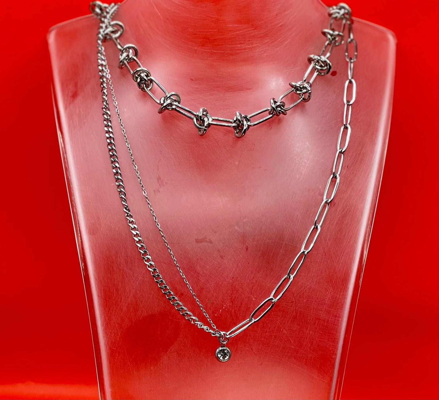 Collane artigianali in acciaio inossidabile LUEUR su busto trasparente, sfondo rosso